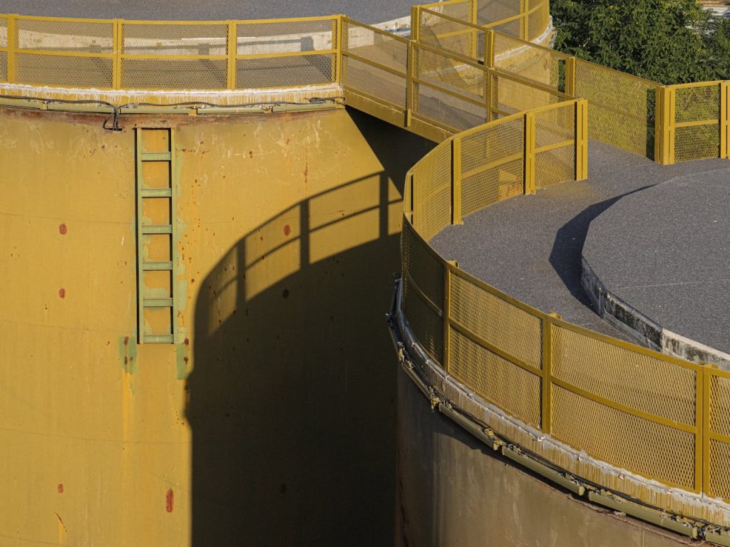 Close-up of a large industrial oil storage tank with yellow railings and ladder.